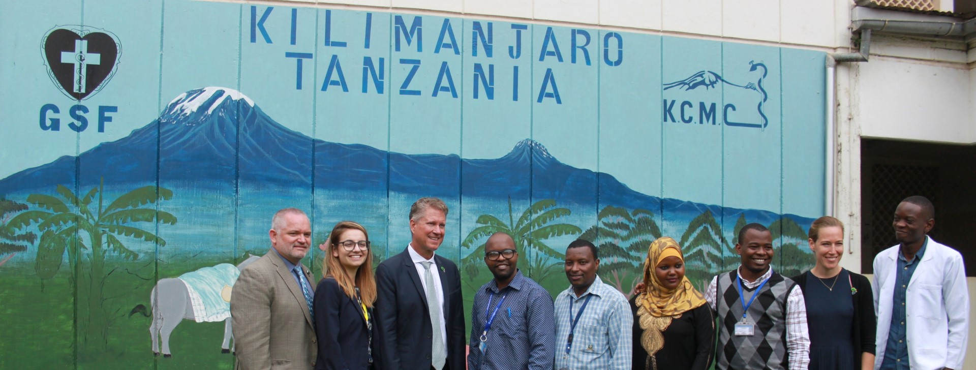 People standing in front of a wall mural that says Kilimanjaro Tanzanie, GSF, KCMC